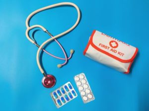 Blue background with a portable first aid kit, stethoscope and some medication in blister pack